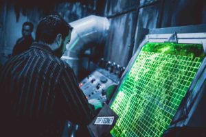 A person in a dark collared shirt looks at a green illuminated map while playing the Aftermath escape room game at Spellbound Escapes.