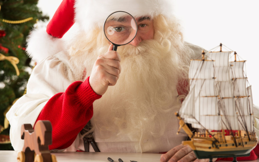 Santa Claus making toys. Looking at camera through the magnifying glass.