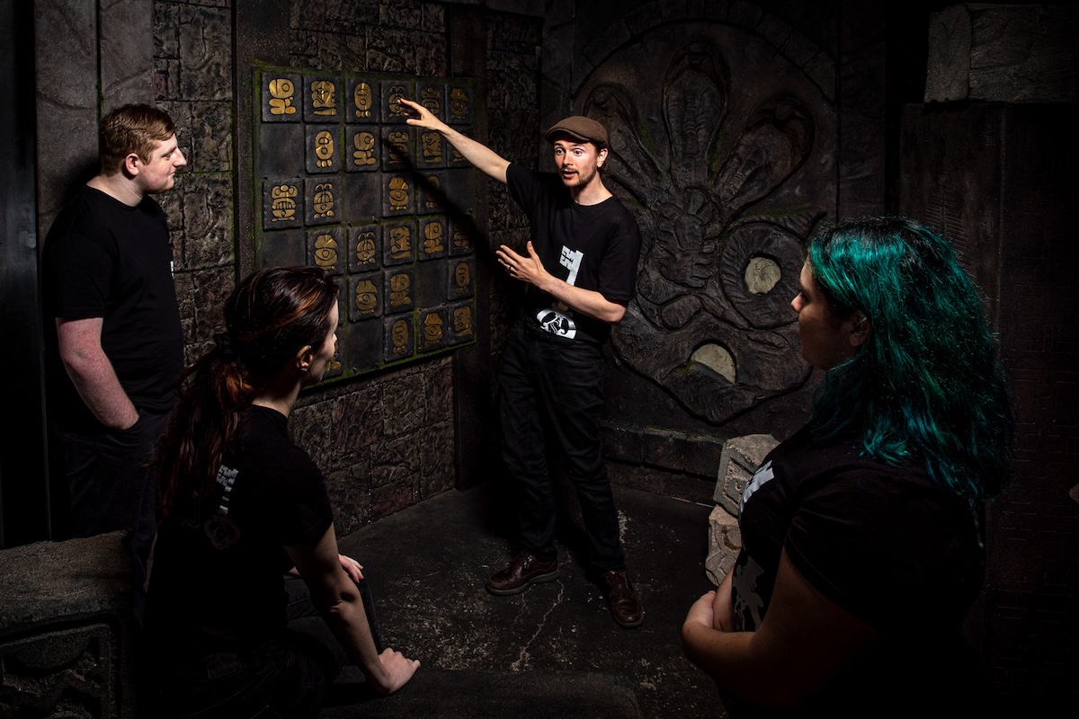 A teambuilding group of 4 people discusses their approach to solving a puzzle in Spellbound's 'Temple of the Laughing God' escape room.